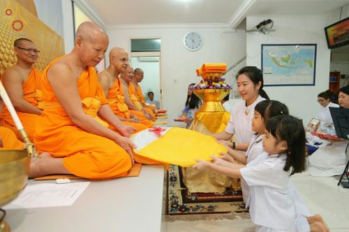 เด็กหญิงและผู้ใหญ่กำลังประเคนผ้ากฐินแด่พระภิกษุสงฆ์ในพิธีทอดกฐินสามัคคี