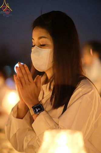 หญิงสาวสวมหน้ากากอนามัยพนมมือด้วยความสงบในพิธีจุดประทีปถวายเป็นพุทธบูชา
