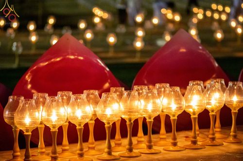 แถวของประทีปในแก้วใสที่จุดไฟสว่างไสววางเรียงรายในพิธีจุดประทีปถวายเป็นพุทธบูชา ณ อนุสรณ์สถานบางปลา