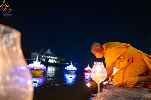 พระภิกษุสวมหน้ากากอนามัยกำลังจุดประทีปในโคมไฟแก้วริมน้ำยามค่ำคืน