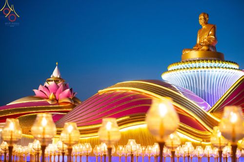 รูปหล่อทองคำพระมงคลเทพมุนีบนฐานอาคารรูปดอกบัวและแสงไฟประทีปในพิธีจุดประทีปถวายเป็นพุทธบูชา