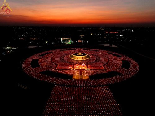 ภาพมุมสูงของพุทธศาสนิกชนจุดประทีปจำนวนมากเป็นวงกลมล้อมรอบอนุสรณ์สถานในช่วงเวลาโพล้เพล้