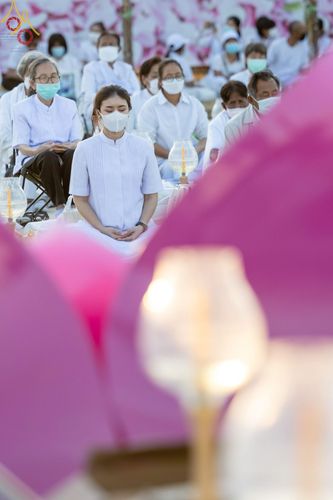กลุ่มพุทธศาสนิกชนสวมชุดขาวนั่งสมาธิท่ามกลางแสงประทีปในพิธีทางศาสนา