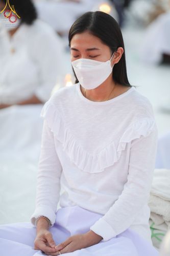 หญิงสาวสวมชุดขาวนั่งหลับตาทำสมาธิในพิธีจุดประทีปถวายเป็นพุทธบูชา