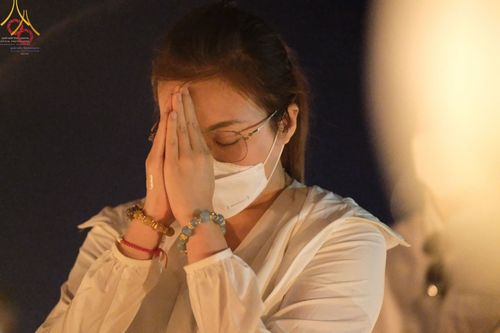 หญิงสาวสวมชุดขาวพนมมือด้วยความศรัทธาในพิธีจุดประทีปถวายเป็นพุทธบูชา