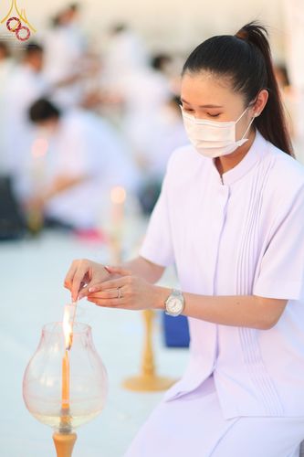 หญิงสาวในชุดขาวกำลังจุดเทียนในโคมแก้วเพื่อประกอบพิธีทางศาสนา