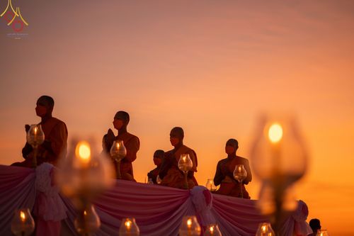 พระภิกษุสงฆ์สวมหน้ากากอนามัยนั่งสมาธิท่ามกลางแสงประทีปในพิธีจุดประทีปถวายเป็นพุทธบูชาช่วงพระอาทิตย์ตกดิน
