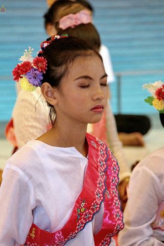 หญิงสาวสวมชุดขาวและสไบสีชมพูประดับดอกไม้ที่ศีรษะกำลังหลับตาทำสมาธิในงานบุญกฐิน