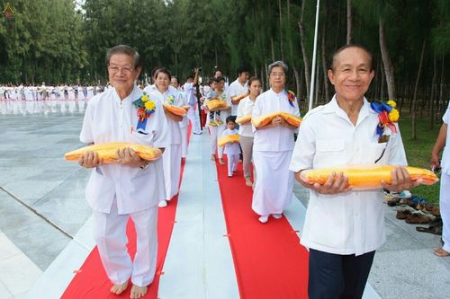 กลุ่มพุทธศาสนิกชนแต่งกายชุดขาวถือผ้าไตรจีวรสีเหลืองทองเดินบนพรมแดงในพิธีทอดกฐิน