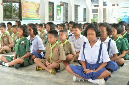 นักเรียนชายหญิงในชุดนักเรียนและชุดลูกเสือเนตรนารีนั่งหลับตาทำสมาธิภายในอาคาร