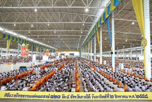 พุทธศาสนิกชนจำนวนมากนั่งเรียงแถวประกอบพิธีถวายไทยธรรมแด่คณะสงฆ์ภายในอาคารขนาดใหญ่