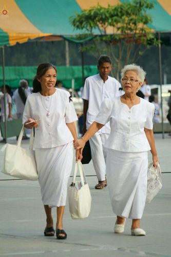 พุทธศาสนิกชนหญิงสองท่านสวมชุดขาวเดินจูงมือกันในงานพิธีกรรมทางศาสนา