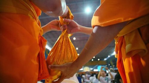 มือของพระสงฆ์ในจีวรสีส้มกำลังประคองถุงผ้าสีทองในพิธีหล่อรูปหล่อทองคำ