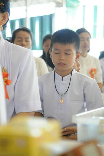 เด็กชายสวมชุดขาวหลับตาทำสมาธิในพิธีตักบาตรฉลองพระภิกษุใหม่