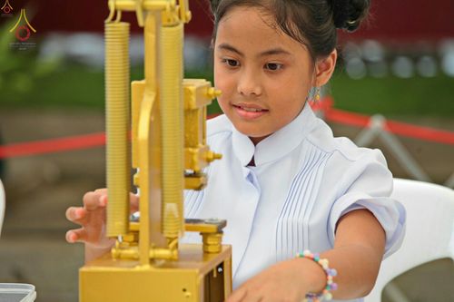เด็กหญิงสวมชุดสีขาวกำลังใช้เครื่องมือพิมพ์พระของขวัญด้วยความตั้งใจในพิธีทางศาสนา