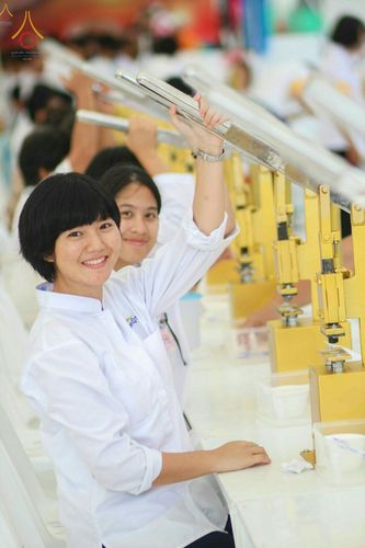 อาสาสมัครหญิงในชุดสีขาวกำลังใช้เครื่องมือกดพิมพ์พระของขวัญ รุ่นบรรลุธรรม ด้วยใบหน้ายิ้มแย้ม