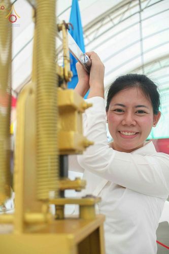 หญิงสาวสวมชุดขาวกำลังใช้เครื่องกดพิมพ์พระของขวัญรุ่นบรรลุธรรมด้วยใบหน้ายิ้มแย้ม