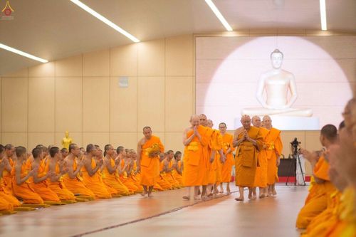 พระภิกษุสงฆ์วัดพระธรรมกายกำลังเดินทำสามีจิกรรมต่อพระเถระผู้ใหญ่ภายในอาคารที่มีฉากหลังเป็นภาพพระพุทธรูป