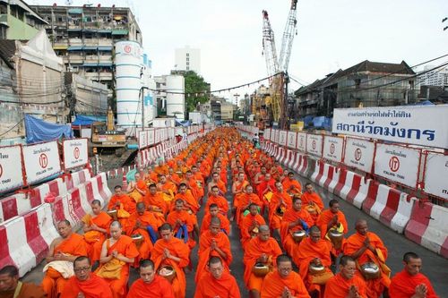 พระสงฆ์จำนวนมากนั่งเรียงแถวบนถนนเจริญกรุงเพื่อรับบิณฑบาตในพื้นที่ก่อสร้างสถานีรถไฟฟ้าใต้ดินวัดมังกร