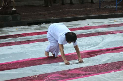 อาสาสมัครหญิงสวมชุดขาวกำลังม้วนพลาสติกปูพื้นบนถนนเพื่อเตรียมจัดงานพิธีตักบาตร