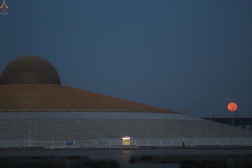 มหาธรรมกายเจดีย์ในยามค่ำคืนที่มีพระจันทร์เต็มดวงสีส้มแดงปรากฏอยู่บนท้องฟ้า