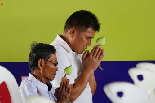 ชายสองคนสวมชุดสีขาวกำลังพนมมือถือดอกบัวเพื่อประกอบพิธีทางศาสนา