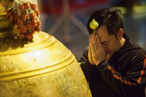 ชายไทยพนมมือถือดอกบัวไหว้ระฆังสีทองขนาดใหญ่ในพิธีทางศาสนา