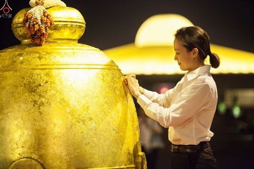 หญิงสาวกำลังปิดแผ่นทองคำเปลวบนระฆังธรรมสีทองขนาดใหญ่ในพิธีทางศาสนา