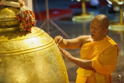 พระสงฆ์กำลังปิดแผ่นทองคำเปลวบนระฆังธรรมสีทองขนาดใหญ่ด้วยความศรัทธา