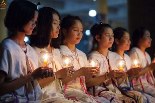 หญิงสาวหลายคนสวมชุดขาวถือโคมเทียนทำสมาธิในพิธีกรรมทางศาสนา