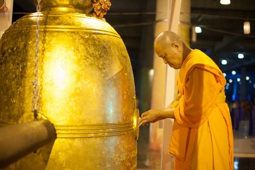 พระสงฆ์กำลังปิดแผ่นทองบนระฆังใบใหญ่สีทองในพิธีกรรมทางศาสนา