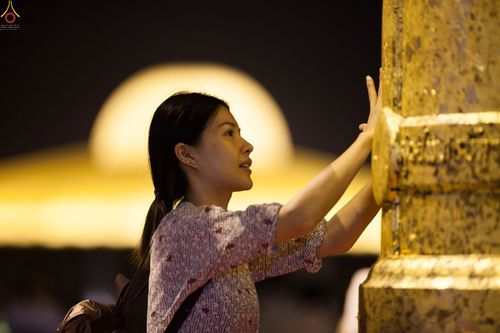 หญิงสาวกำลังปิดแผ่นทองบนระฆังธรรมในพิธีทางศาสนาช่วงเวลากลางคืน