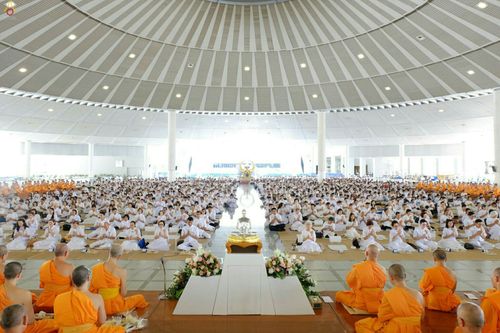 พุทธศาสนิกชนชุดขาวจำนวนมากนั่งปฏิบัติธรรมร่วมกับพระภิกษุสงฆ์ภายในอาคารทรงกลมขนาดใหญ่