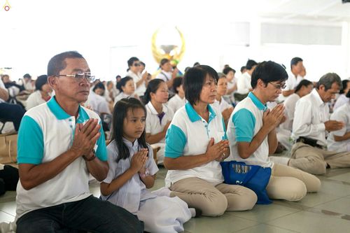 กลุ่มพุทธศาสนิกชนนั่งพนมมือประกอบพิธีกรรมทางศาสนาในอาคาร