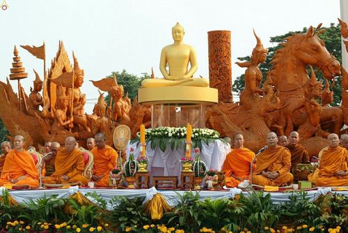 พระสงฆ์นั่งสมาธิเรียงแถวหน้าพระพุทธรูปและประติมากรรมเทียนพรรษาแกะสลัก