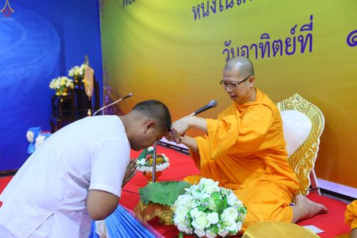 พระภิกษุสงฆ์กำลังใช้กรรไกรตัดปอยผมให้แก่ชายชุดขาวในพิธีอุปสมบทหมู่