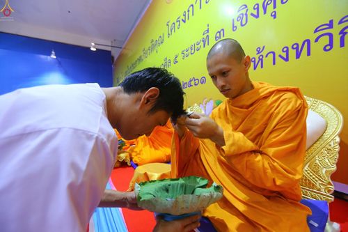 พระภิกษุสงฆ์กำลังใช้กรรไกรตัดปอยผมให้แก่ชายในชุดขาวเพื่อเตรียมตัวเข้าพิธีอุปสมบท