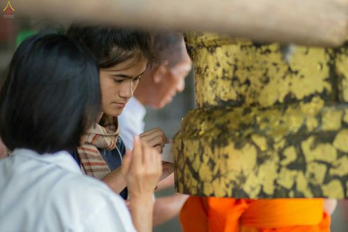 พุทธศาสนิกชนกำลังใช้แผ่นทองคำเปลวปิดลงบนระฆังธรรมสีทองด้วยความตั้งใจ