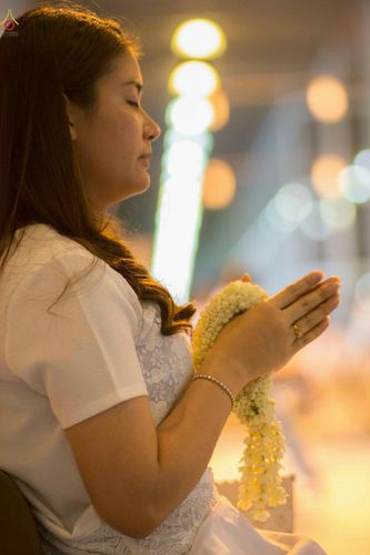 หญิงสาวสวมชุดขาวพนมมือถือพวงมาลัยดอกมะลิด้วยความศรัทธาในงานพิธีทางศาสนา