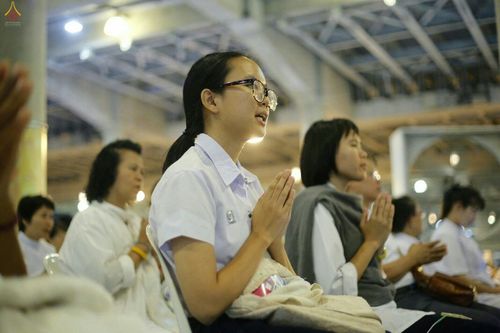 นักเรียนหญิงและพุทธศาสนิกชนพนมมือสวดมนต์ในพิธีทางศาสนา