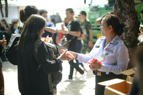 เจ้าหน้าที่ในเครื่องแบบกำลังยื่นถุงอาหารและน้ำดื่มให้กับประชาชนที่มาสักการะพระบรมศพฯ