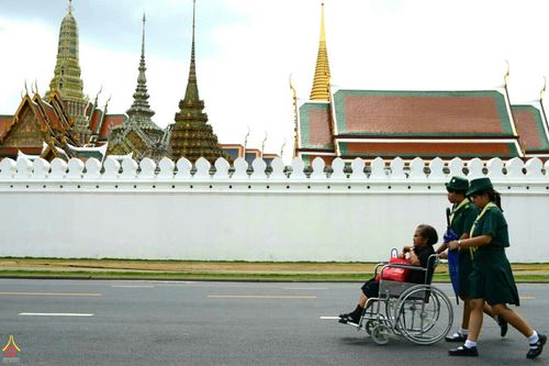 ลูกเสือหญิงช่วยเข็นรถเข็นผู้สูงอายุบริเวณหน้ากำแพงพระบรมมหาราชวัง