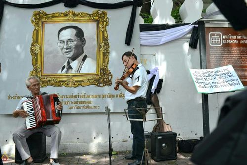 นักดนตรีชายสองคนกำลังเล่นดนตรีสดหน้าพระบรมฉายาลักษณ์เพื่อถวายความอาลัย