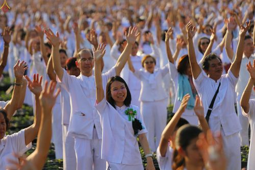 กลุ่มพุทธศาสนิกชนในชุดขาวกำลังชูมือขึ้นในกิจกรรมปลูกต้นเบญจทรัพย์ที่วัดพระธรรมกาย