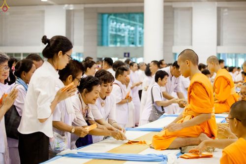 พุทธศาสนิกชนในชุดขาวกำลังถวายปัจจัยบูชาธรรมแด่พระภิกษุสงฆ์ภายในอาคารวัดพระธรรมกาย