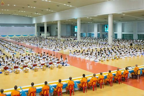 พุทธศาสนิกชนจำนวนมากในชุดขาวนั่งร่วมพิธีปุพพเปตพลีภายในอาคาร โดยมีพระภิกษุสงฆ์นั่งประกอบพิธีอยู่ด้านหน้า