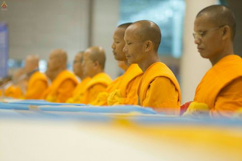 พระภิกษุสงฆ์ห่มจีวรสีเหลืองทองกำลังนั่งหลับตาทำสมาธิเรียงแถวกันอย่างเป็นระเบียบในพิธีทางศาสนา