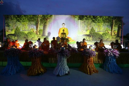 พระภิกษุสงฆ์นั่งบนเวทีในพิธีบรรพชาสามเณร จังหวัดเลย มีฉากหลังเป็นภาพพระพุทธรูปและป่าไม้ในยามค่ำคืน