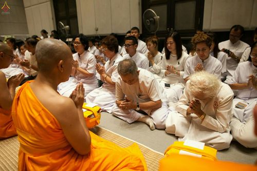 กลุ่มพุทธศาสนิกชนในชุดขาวนั่งพนมมือฟังพระสงฆ์ในพิธีบรรพชาอุปสมบทหมู่นาคธรรมทายาท