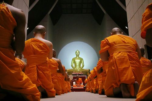 พระภิกษุสงฆ์จำนวนมากนั่งคุกเข่ากราบพระพุทธรูปทองคำภายในอาคารปฏิบัติธรรม